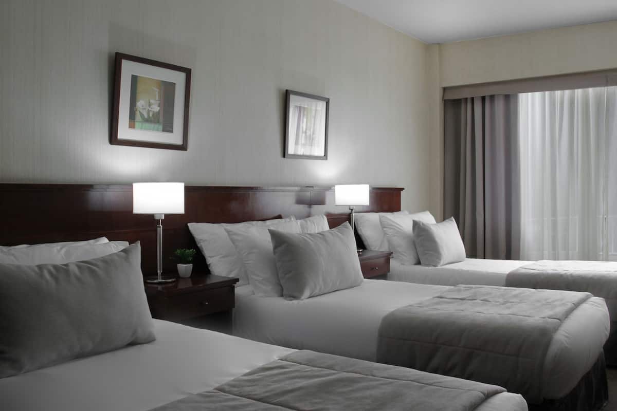 A hotel room with two beds, a nightstand with a lamp, and a window with curtains.