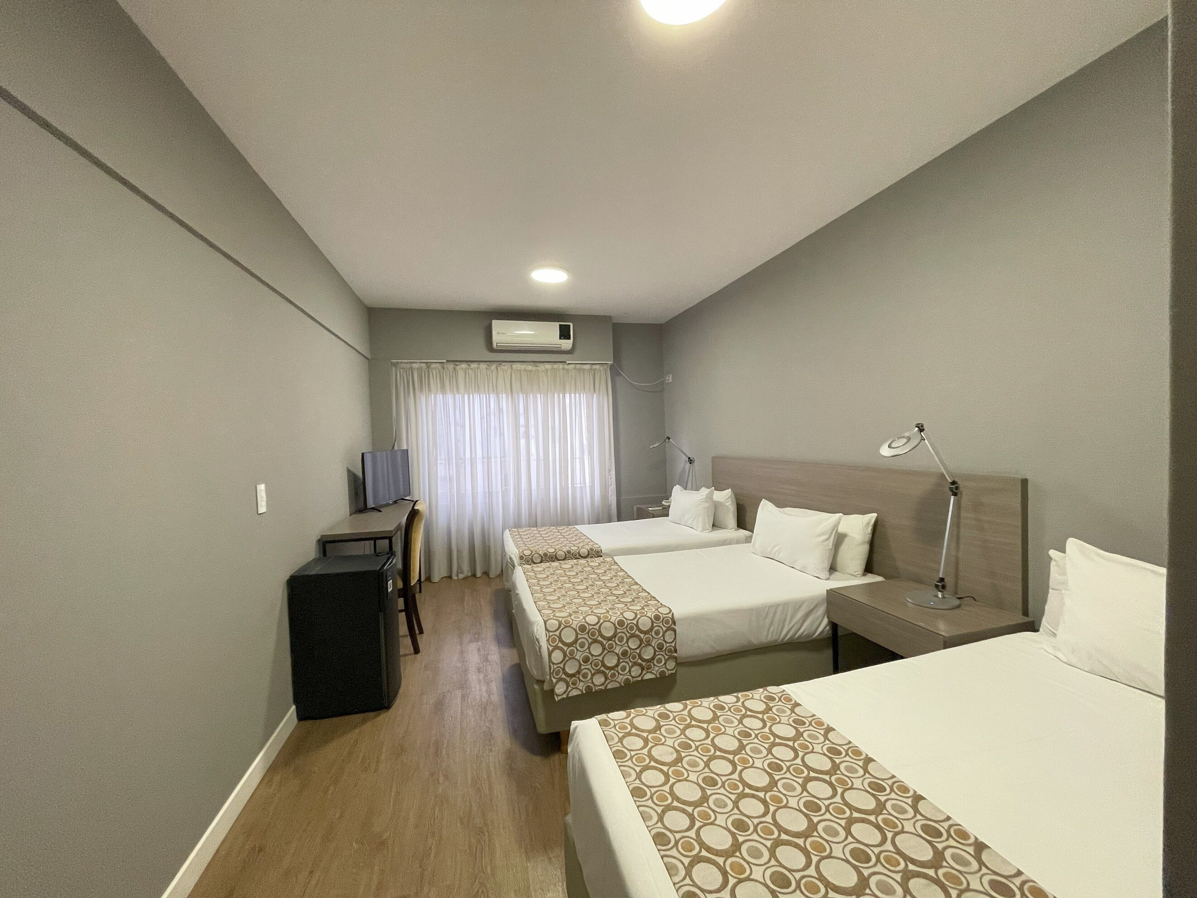 Ein Hotelzimmer mit zwei Betten, einem Schreibtisch, einem Stuhl, einem Fernseher und einer Klimaanlage.
