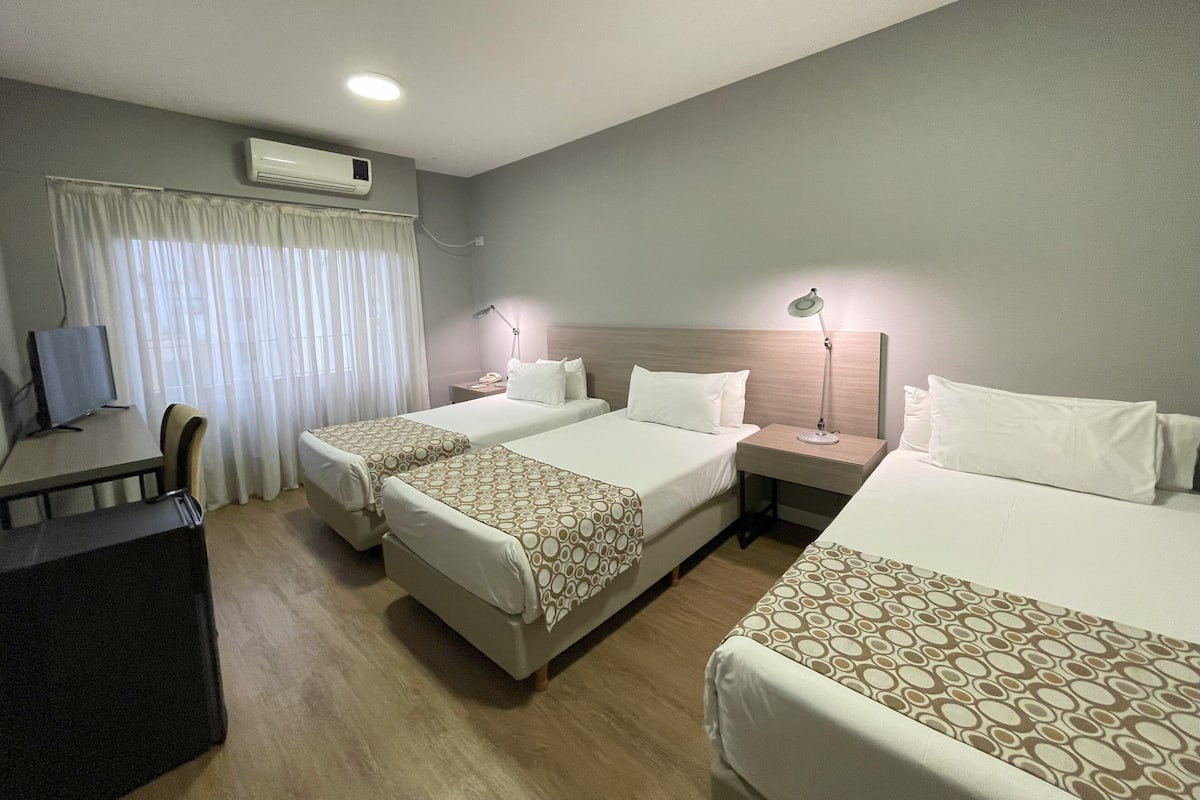 A hotel room with two beds, a desk, a chair, a TV, and an air conditioning unit.