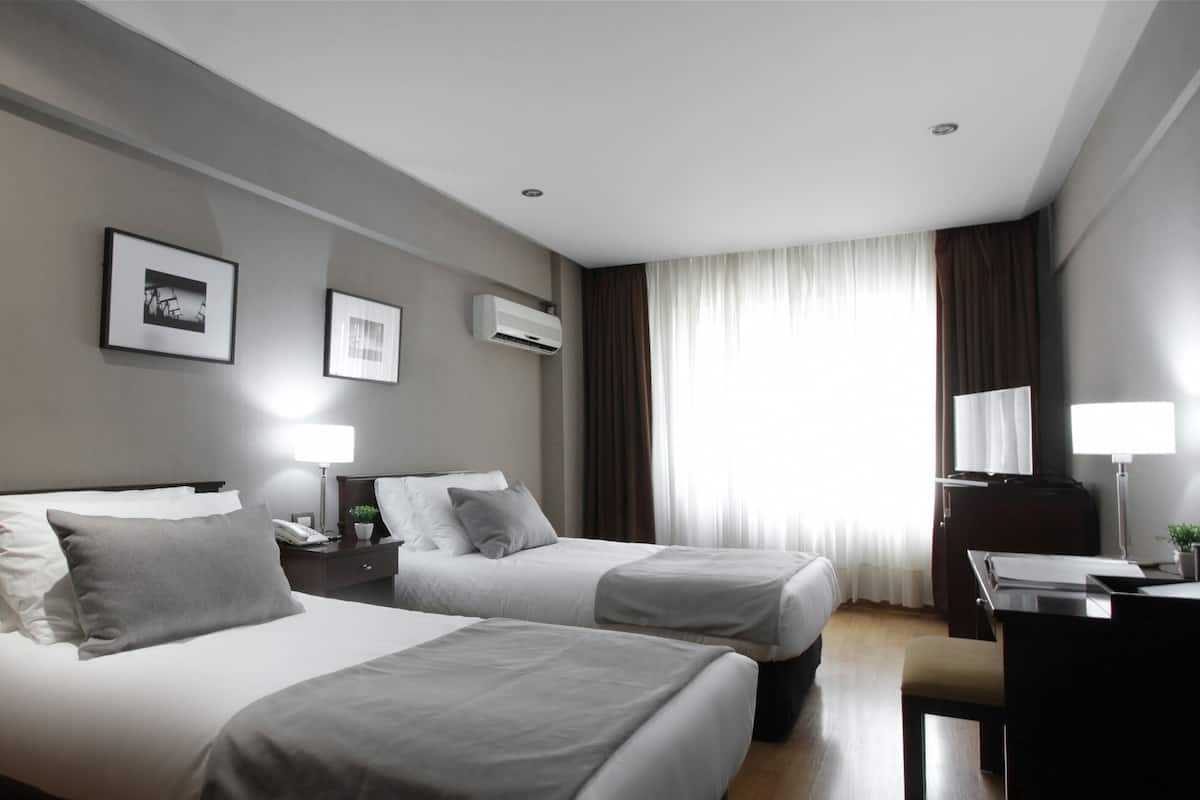 A hotel room with two beds, a desk, a chair, a lamp, and a window with curtains.