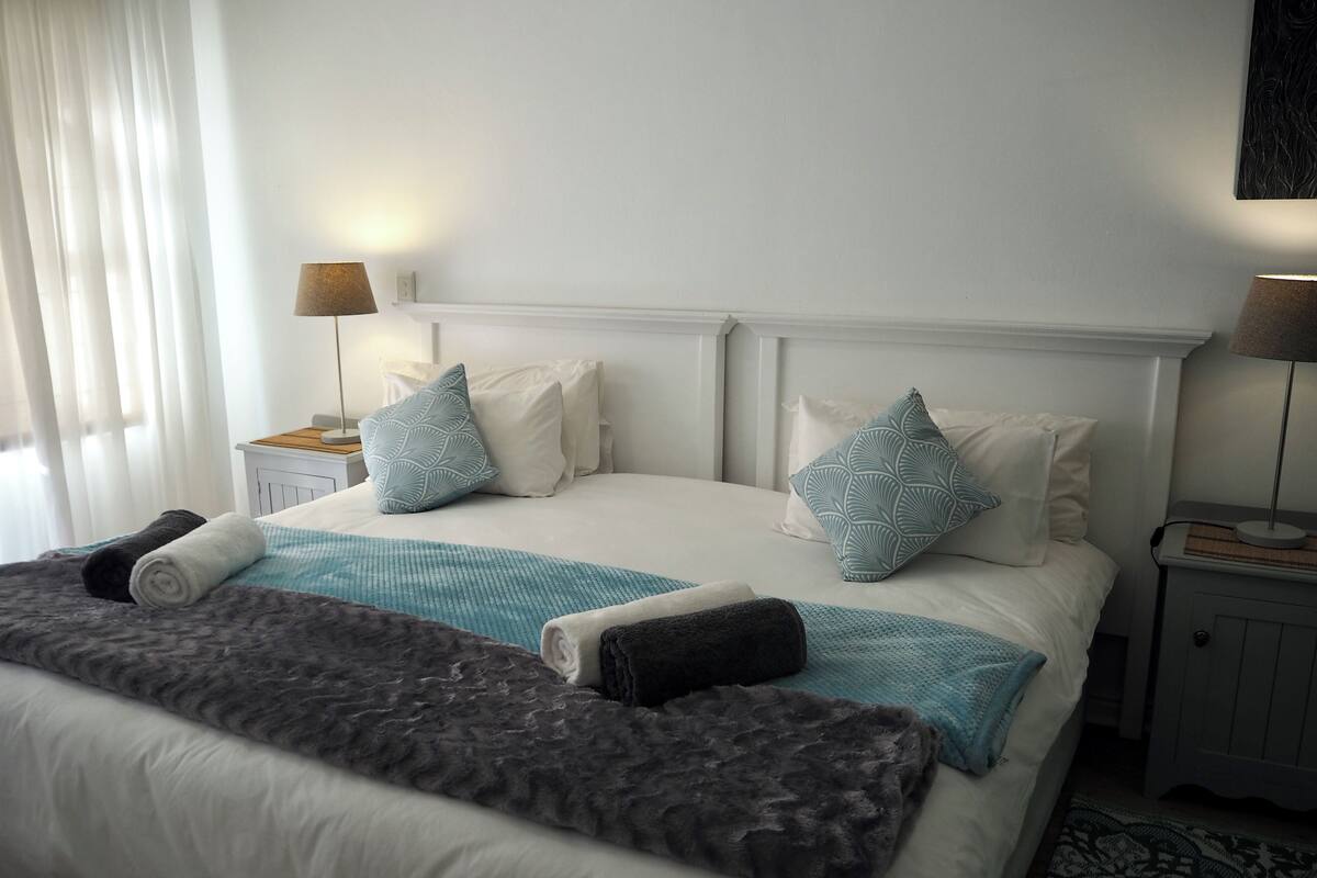 Ein ordentlich bezogenes Bett mit einer gemusterten Tagesdecke, Kissen und einer Decke. Es gibt zwei Nachttische mit Lampen.