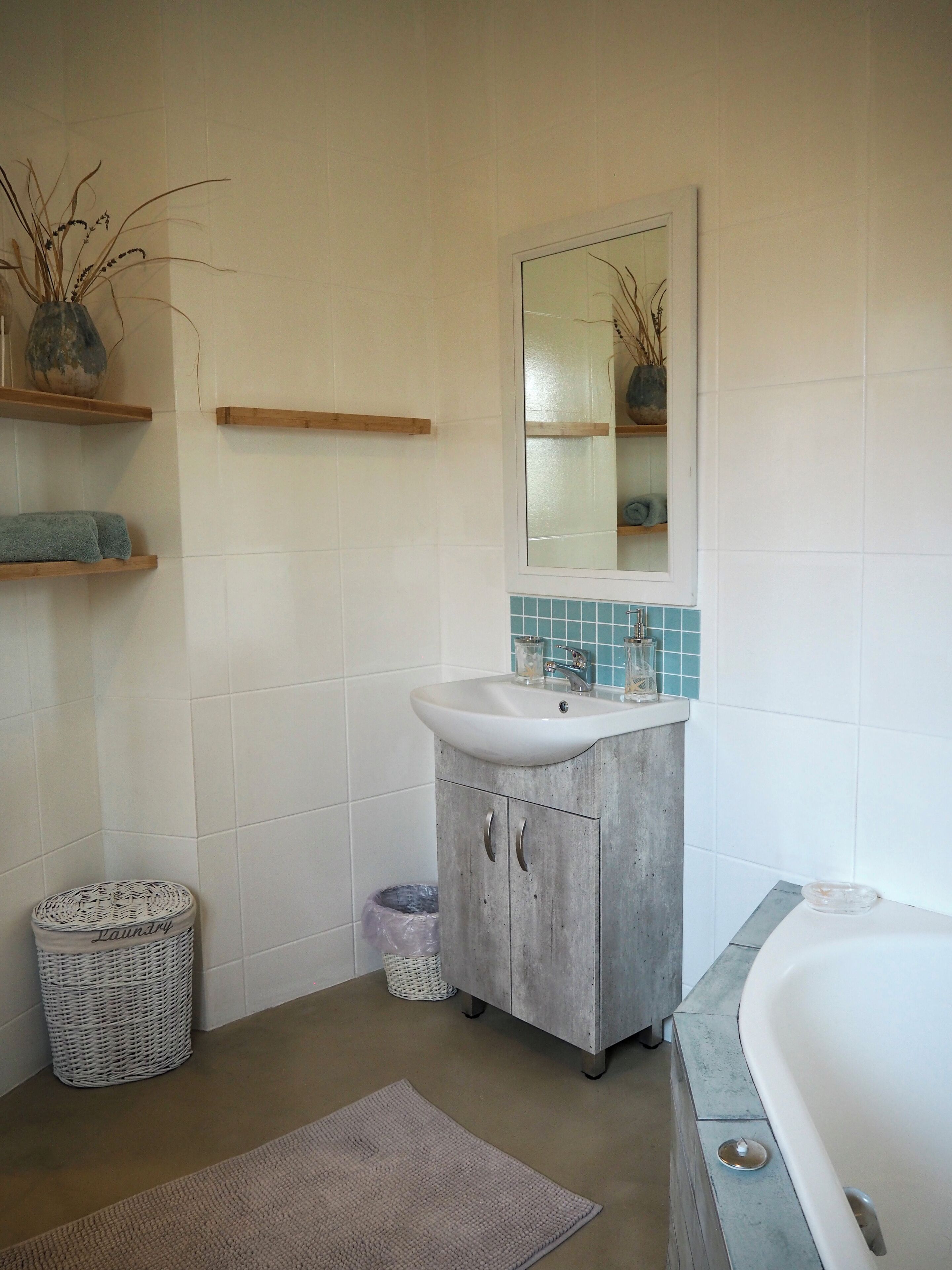 Un baño con lavamanos blanco, un espejo, una bañera y un estante pequeño con una planta.