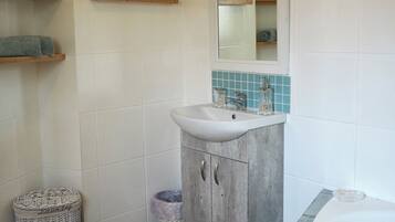 Un baño con lavamanos blanco, un espejo, una bañera y un estante pequeño con una planta.