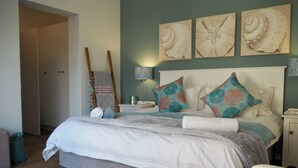 Quarto bem arrumado com cama, almofadas, mesa de cabeceira, abajur e obras de arte na parede.
