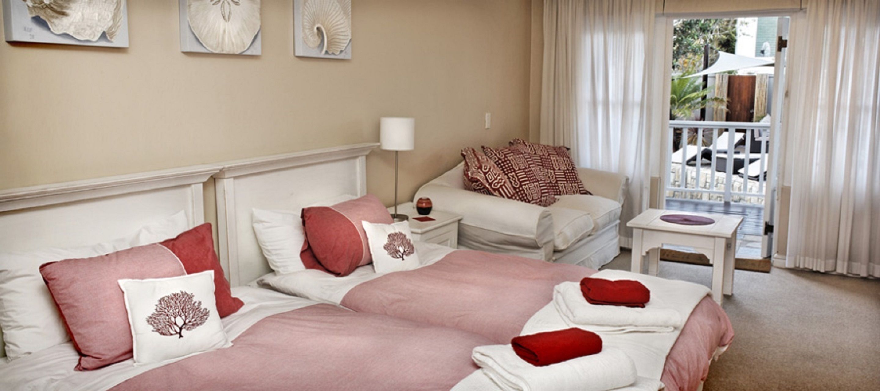Habitación de hotel con una cama grande, dos mesitas de noche, una mesita pequeña y un balcón con vistas.