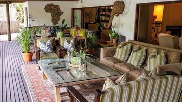 A cozy outdoor seating area with a wooden deck, cushioned sofas, and potted plants.