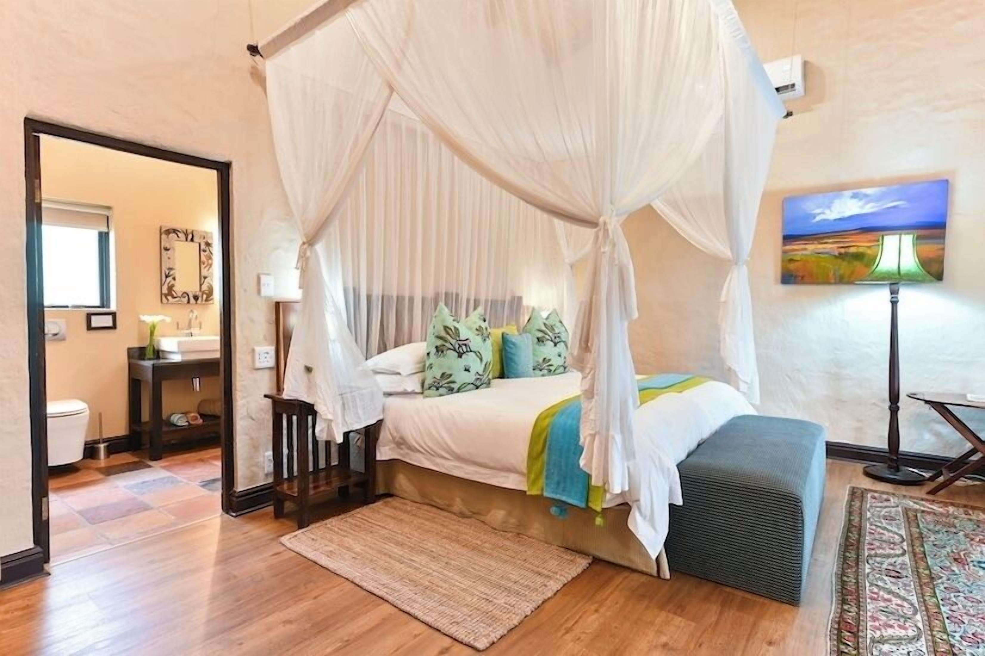 A bedroom with a canopy bed, a bedside lamp, and a view of the bathroom.