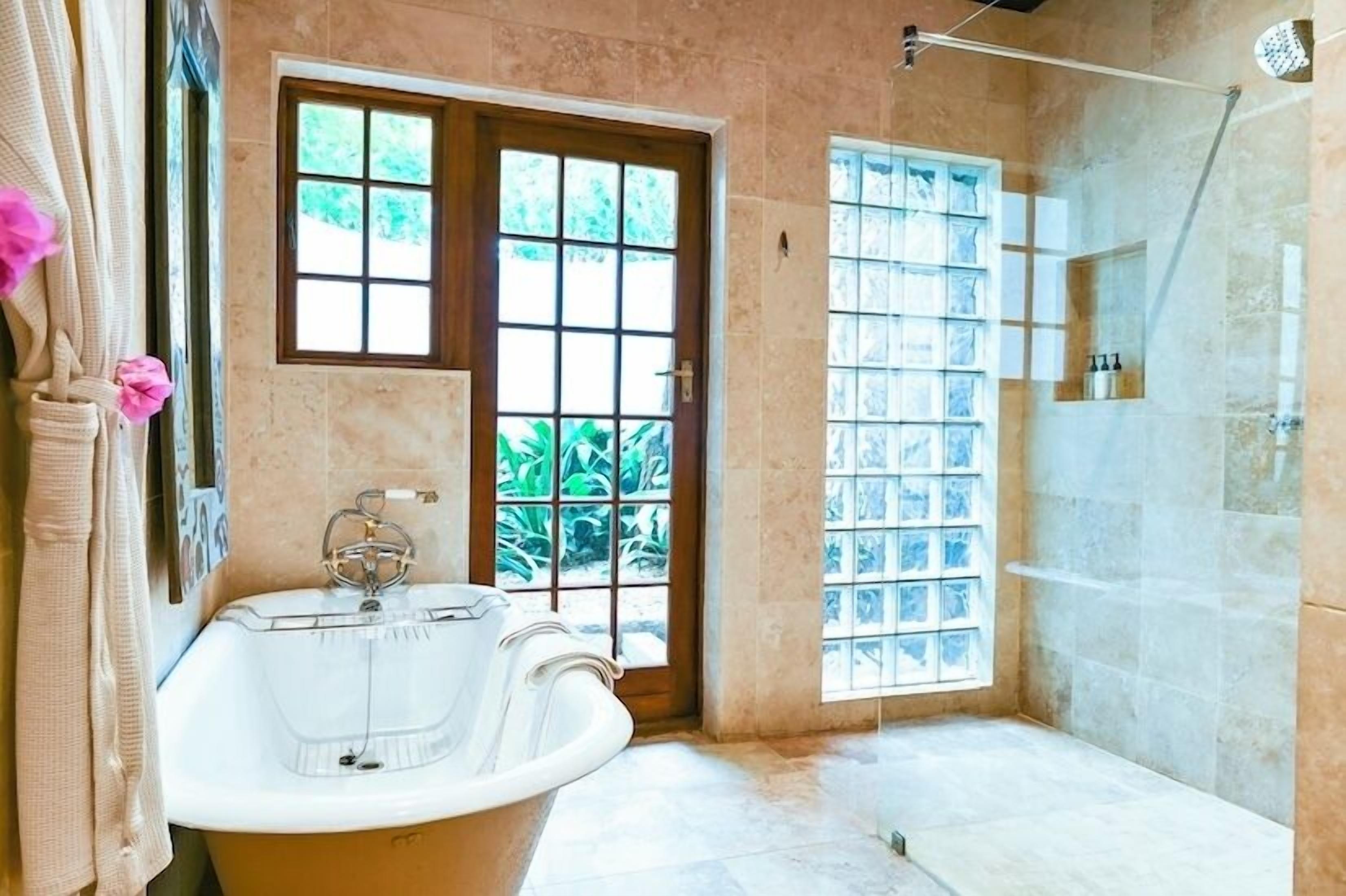 Un baño con bañera, ducha y ventana con vistas al verdor.