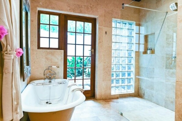 A bathroom with a bathtub, a shower, and a window with a view of greenery.