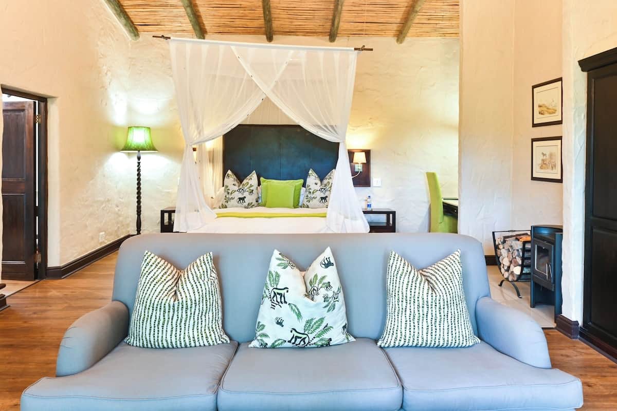 A bedroom with a canopy bed, a sofa with patterned cushions, and a bedside table with a lamp.
