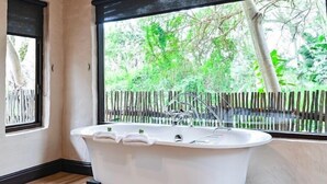 Une salle de bain moderne avec une baignoire sur pieds, une fenêtre donnant sur un espace verdoyant et un plancher en bois.