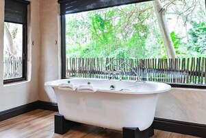 Casa de banho moderna com uma banheira independente, janela com vista para vegetação e chão de madeira.