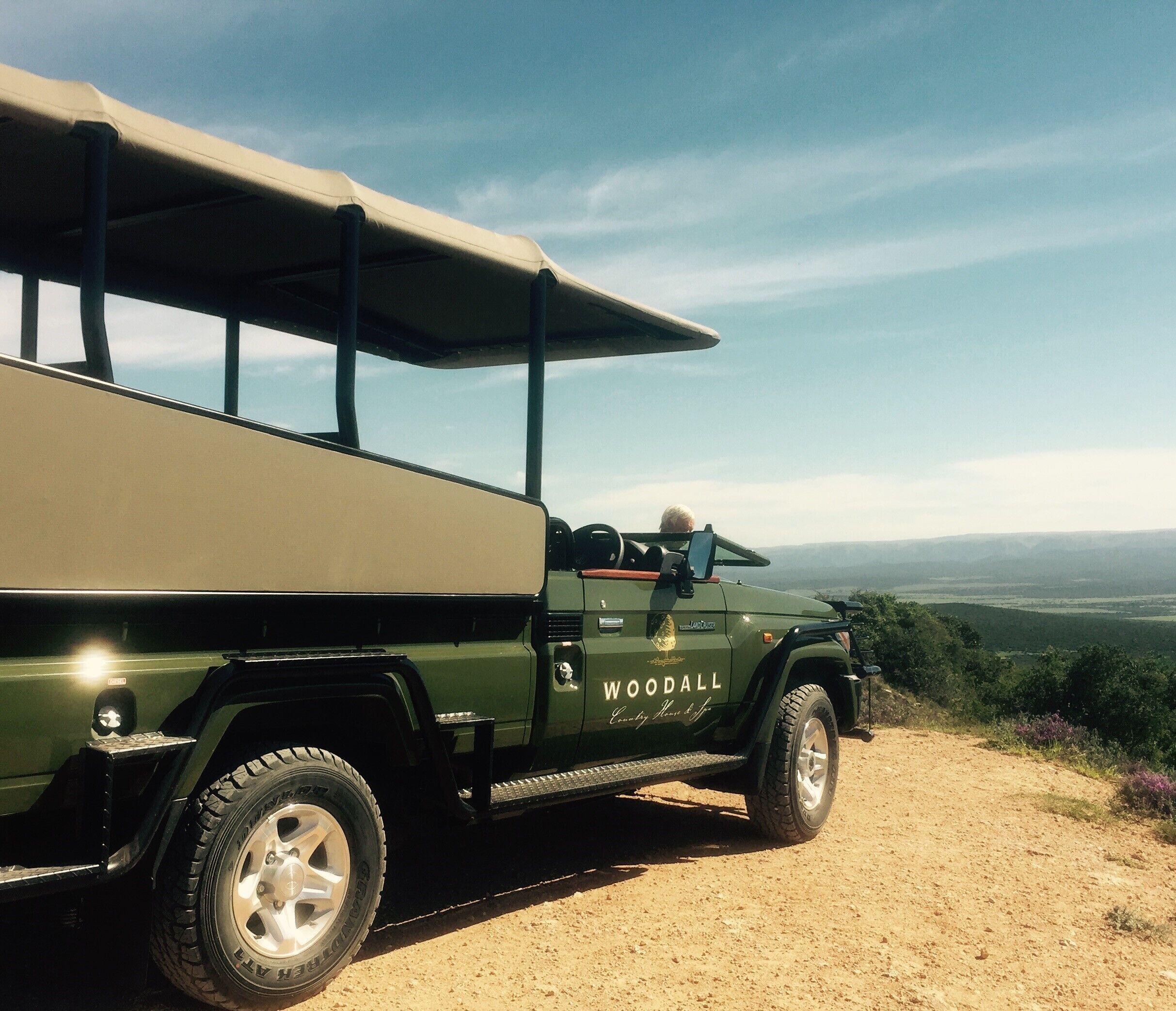 Un vehículo todoterreno verde con portaequipajes estacionado en un camino de tierra con una vista panorámica al fondo.