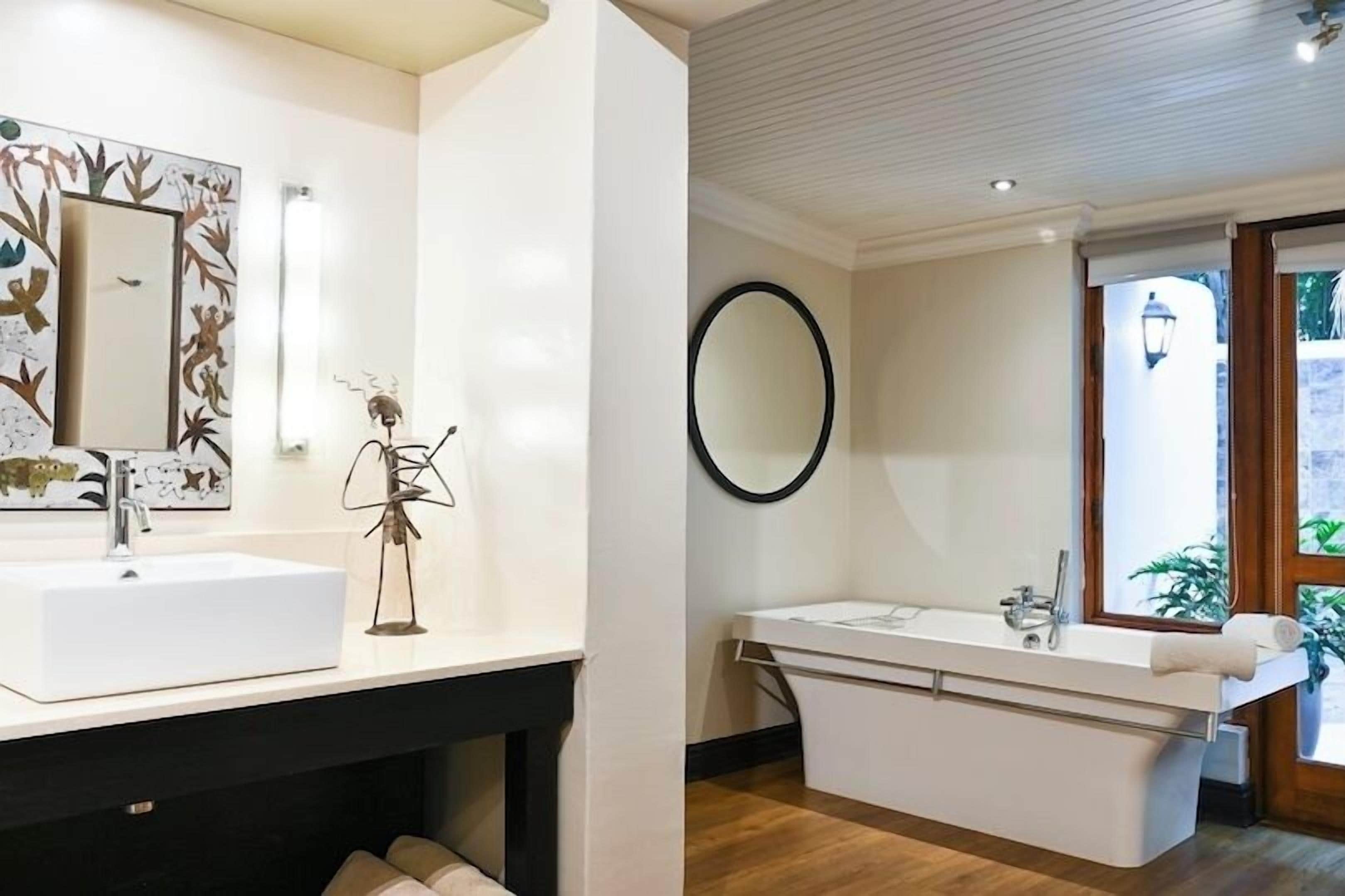 Un baño moderno con un lavamanos grande de color blanco, un espejo redondo y una bañera.