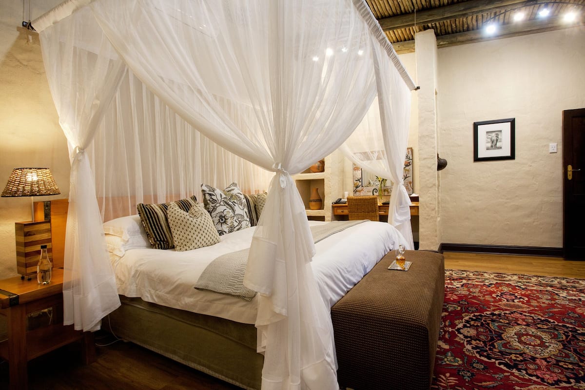 A bedroom with a canopy bed, bedside tables, a lamp, a rug, and a framed picture on the wall.
