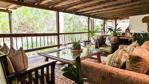 Un espace extérieur abrité, aménagé avec du mobilier en bois, des tables en verre et des plantes en pot.