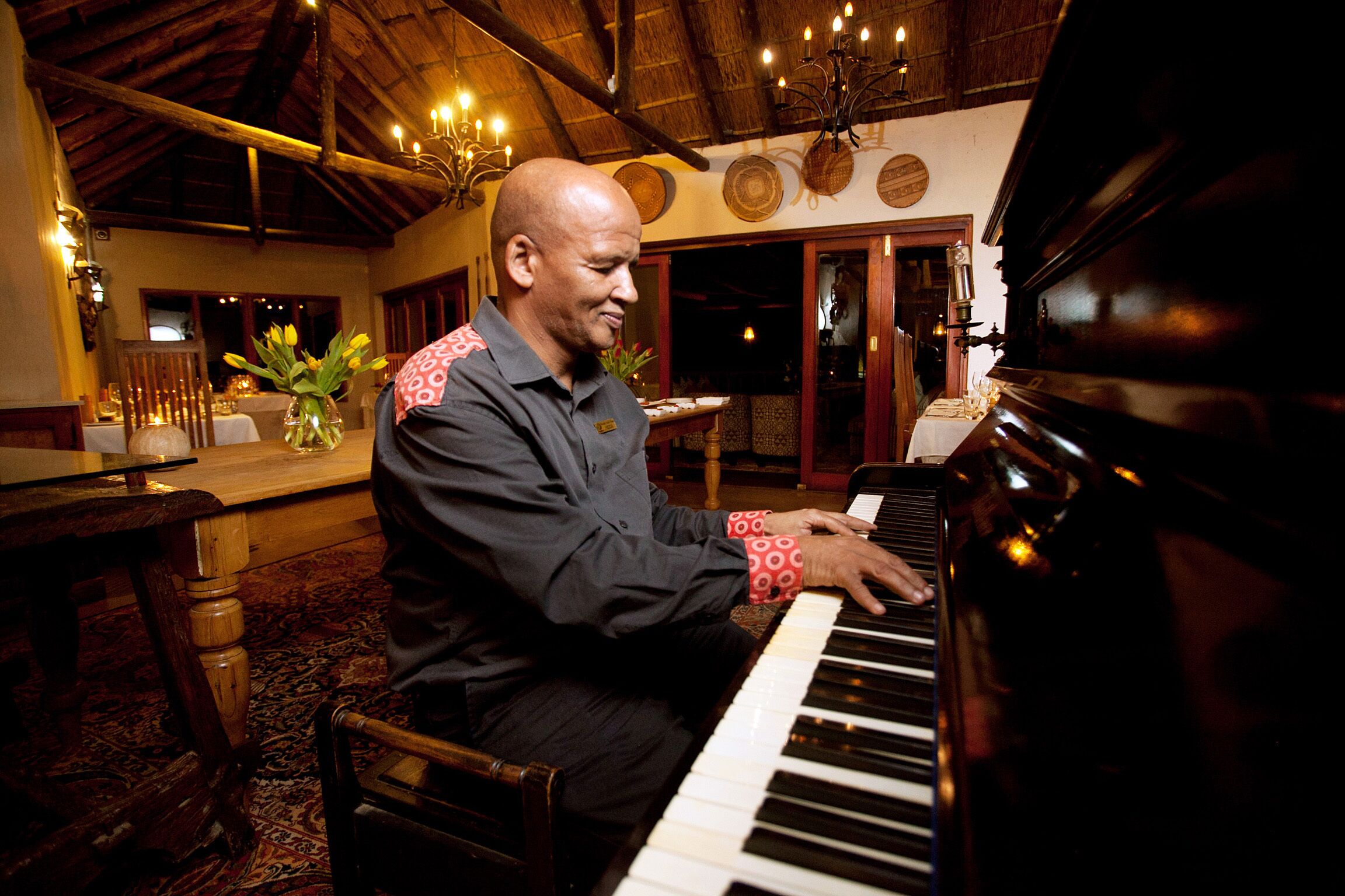 Un hombre tocando el piano en una habitación con muebles de madera y una araña.