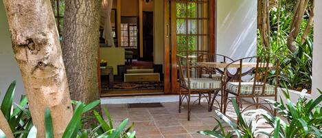 Uma área de pátio com mesa e cadeiras, rodeada por plantas e uma grande árvore.