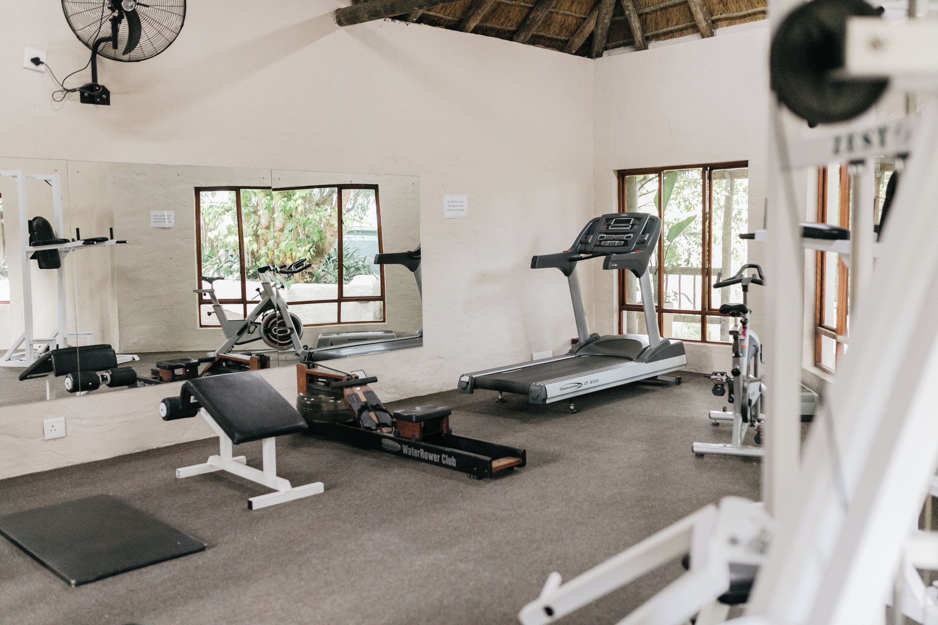 Une salle de sport équipée d’un tapis de course, d’un rameur et d’un banc de musculation.