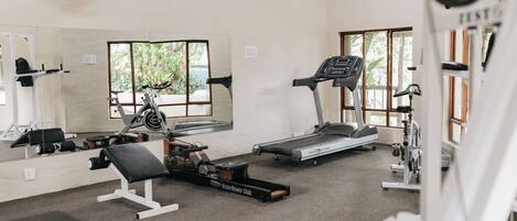 Une salle de sport équipée d’un tapis de course, d’un rameur et d’un banc de musculation.