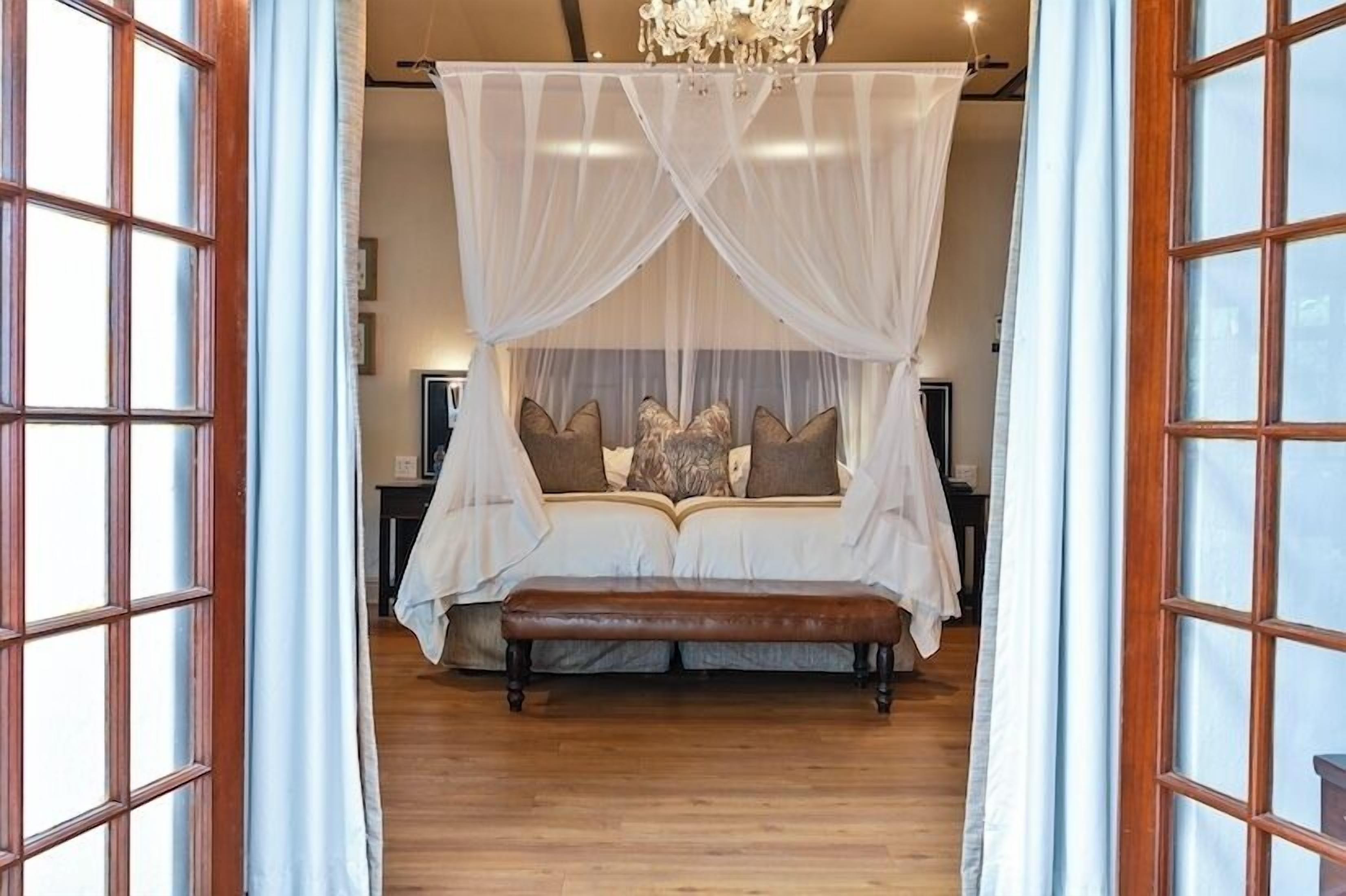 Un dormitorio con cama con dosel, suelo de madera y un banco al pie de la cama.