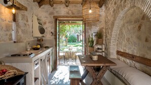 A rustic kitchen with a stone wall, wooden beams, and a view to a garden. - Paliokaliva Village (Zakynthos)