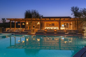 A poolside area with lounge chairs and a bar area with seating and a kitchen visible through the glass. - Paliokaliva Village (Zakynthos)