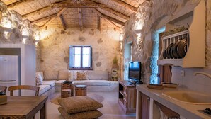 A rustic stone interior with a wooden ceiling, a sofa, a television, and a kitchen area. - Paliokaliva Village (Zakynthos)