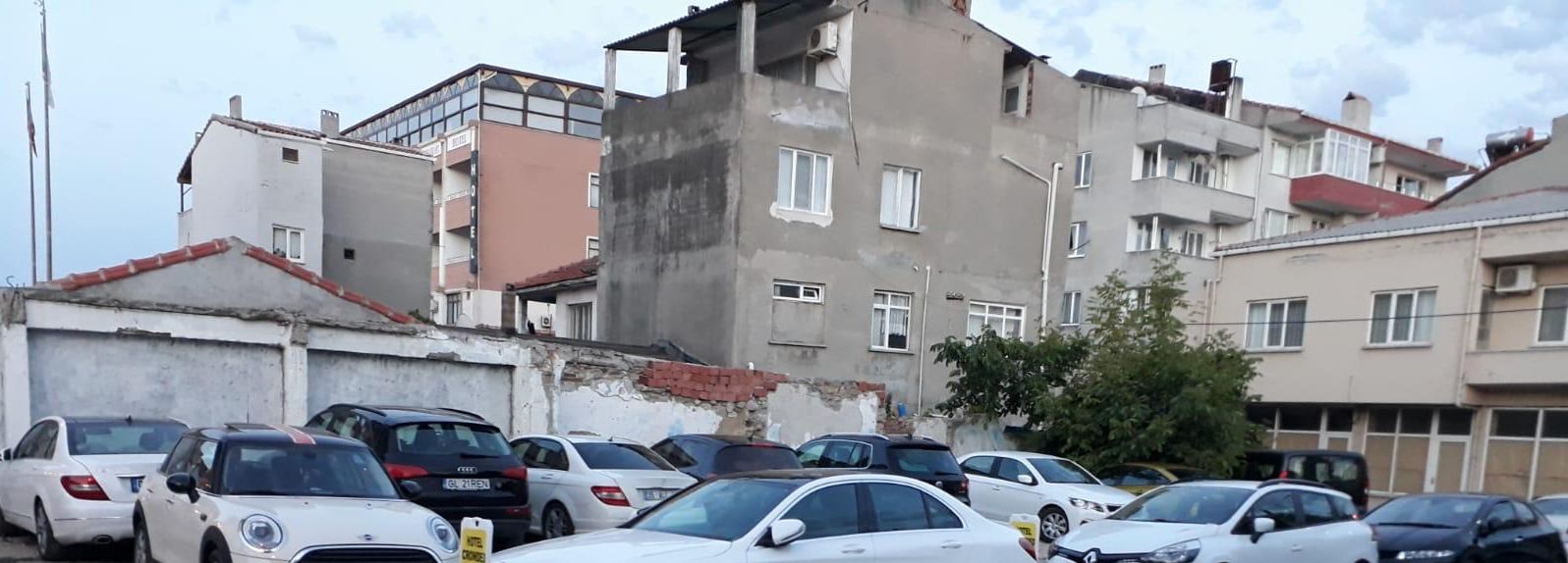 Un estacionamiento con varios autos, un edificio de techo rojo y una construcción a medio hacer.