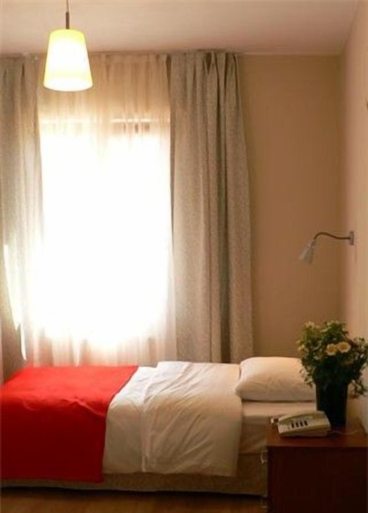 Une chambre à coucher avec un lit, une table de chevet avec un téléphone, une lampe et une fenêtre avec des rideaux.