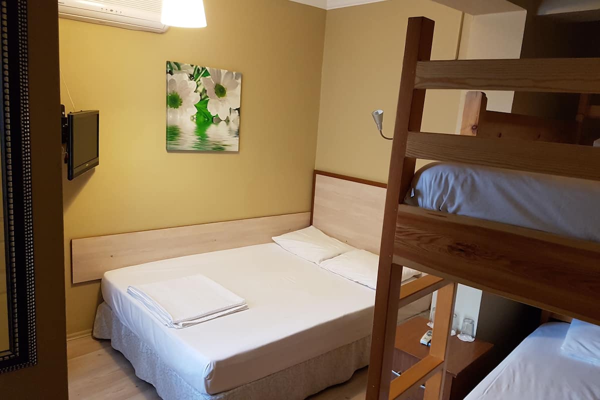 A bunk bed room with a single bed, a bedside table, a lamp, and a painting on the wall.