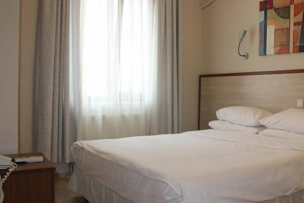 A hotel room with a large bed, a bedside telephone, and a painting on the wall.