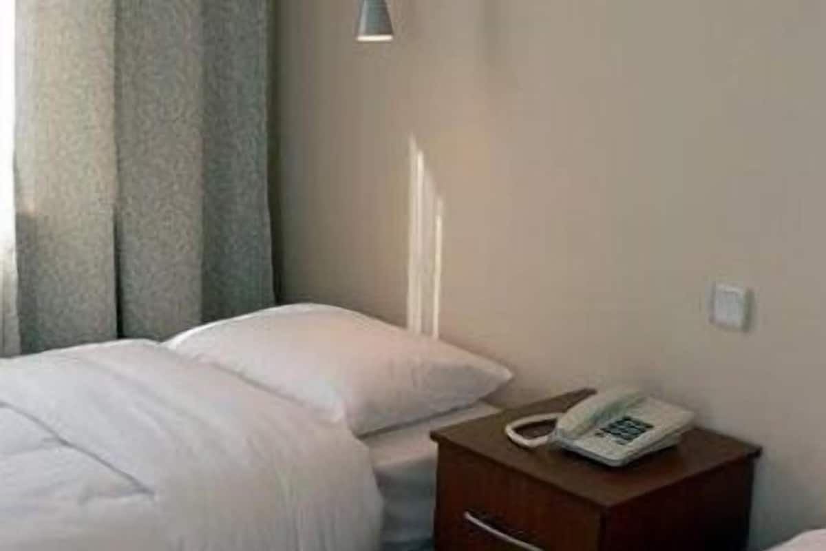 A hotel room with two beds, a bedside table with a phone, and a wall-mounted lamp.