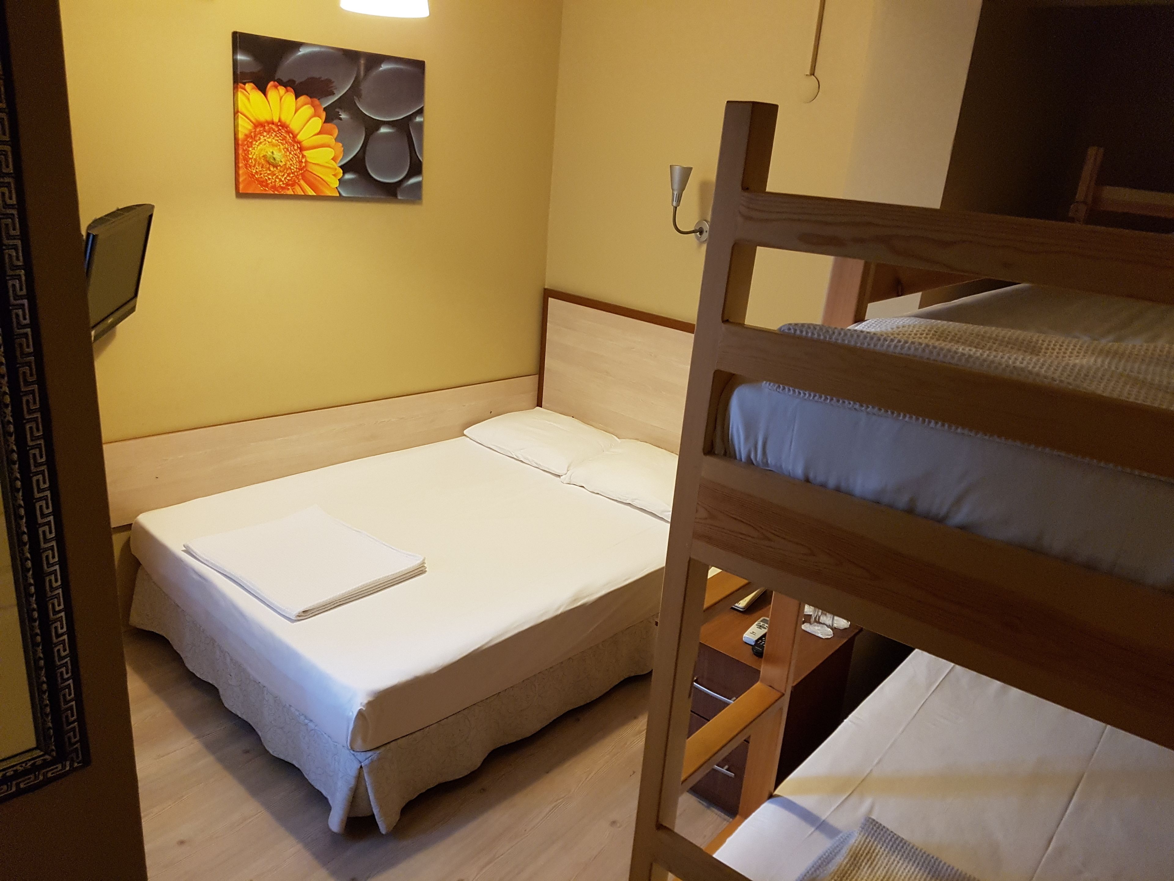 Un lit simple avec une tête de lit en bois, une table de chevet avec une lampe et un tableau représentant des fleurs accroché au mur.