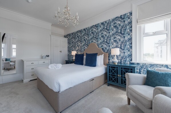 Une chambre à coucher avec un grand lit, une commode, une chaise, une table de chevet et une fenêtre donnant sur un beau paysage.
