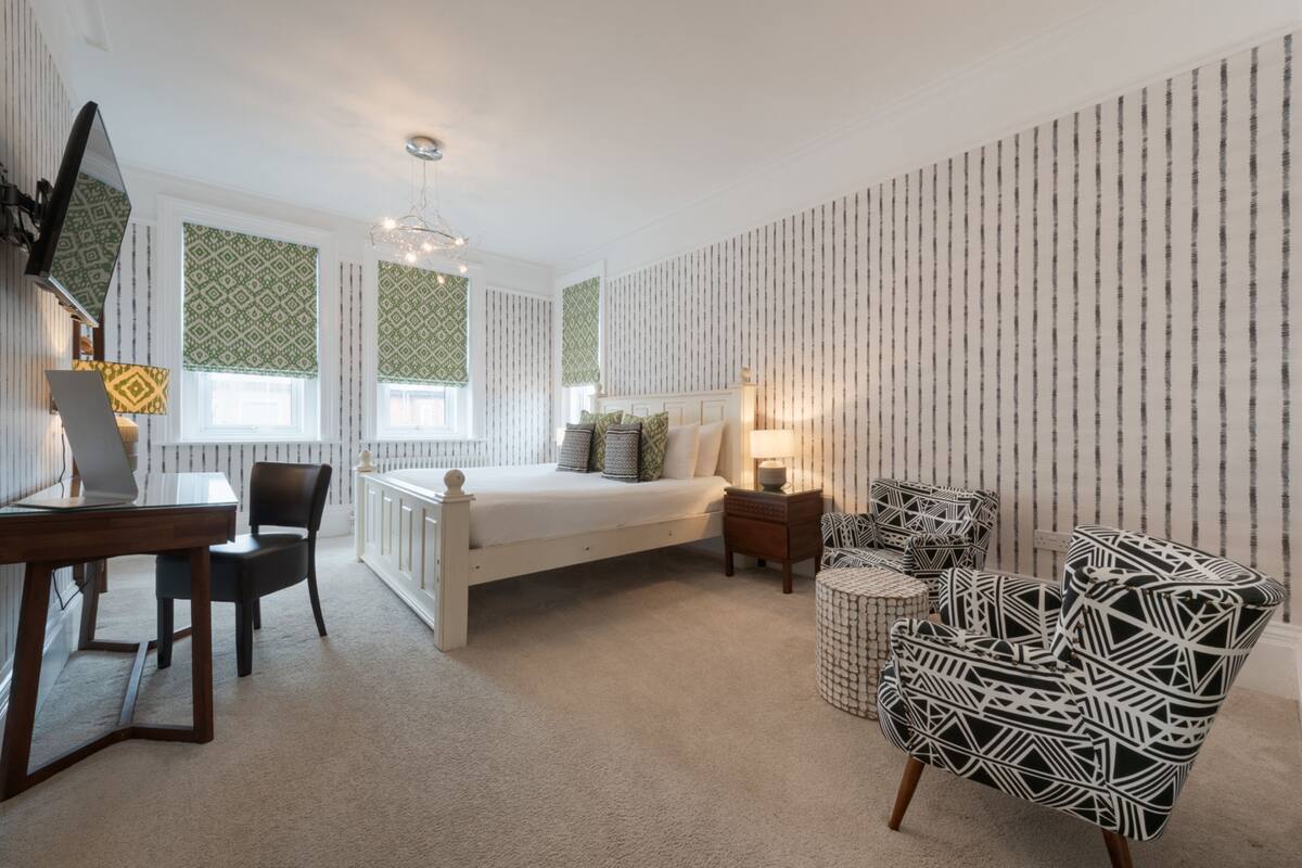 Un dormitorio con cama, escritorio, silla y sillón estampado.