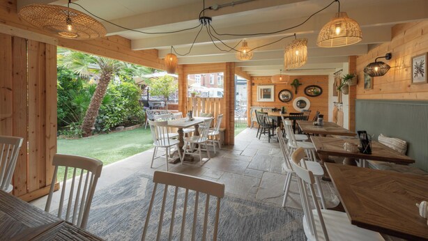 Un restaurante con interiores de madera, mesas al aire libre e iluminación colgante de mimbre.