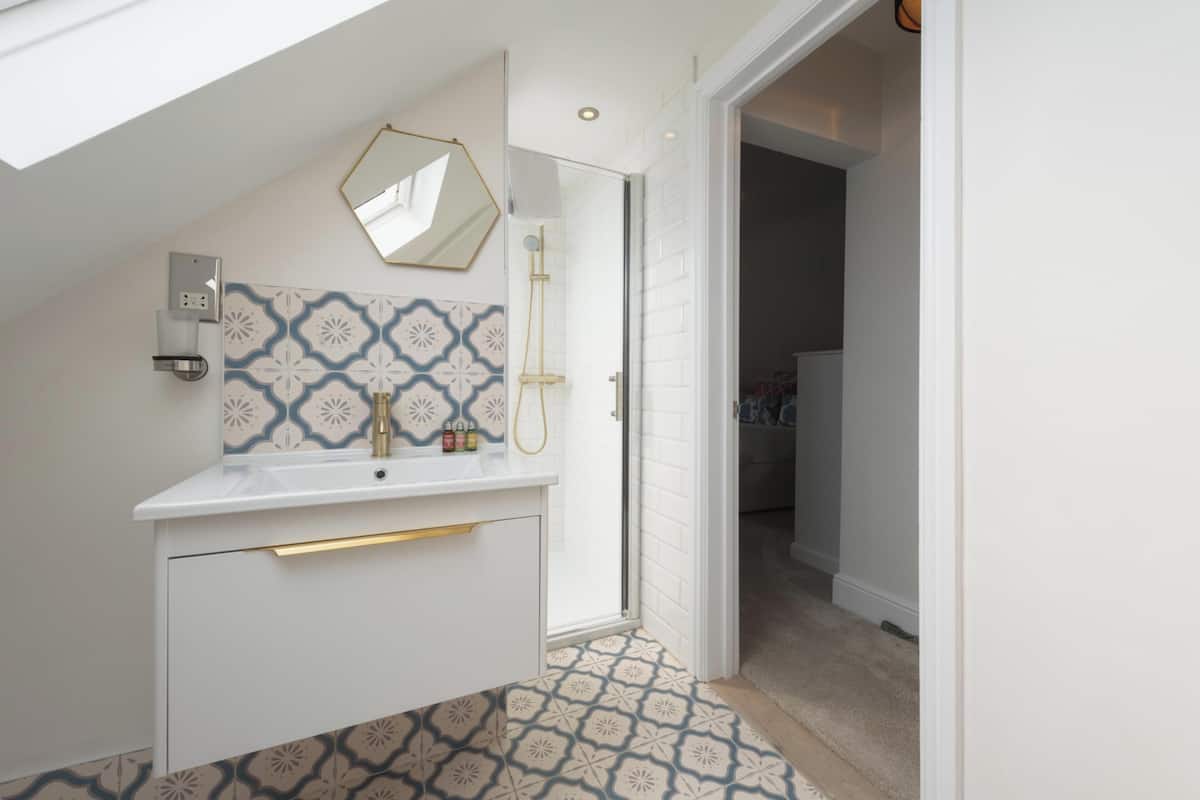 Un baño moderno con tocador blanco, ducha, azulejos estampados y tragaluz.