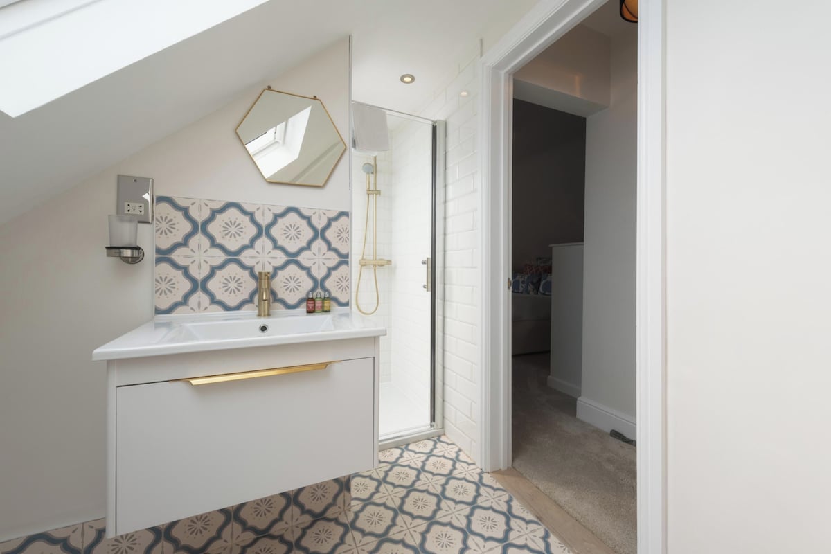 Une salle de bain moderne avec un meuble-lavabo blanc, une douche, des carreaux à motifs et un puits de lumière.
