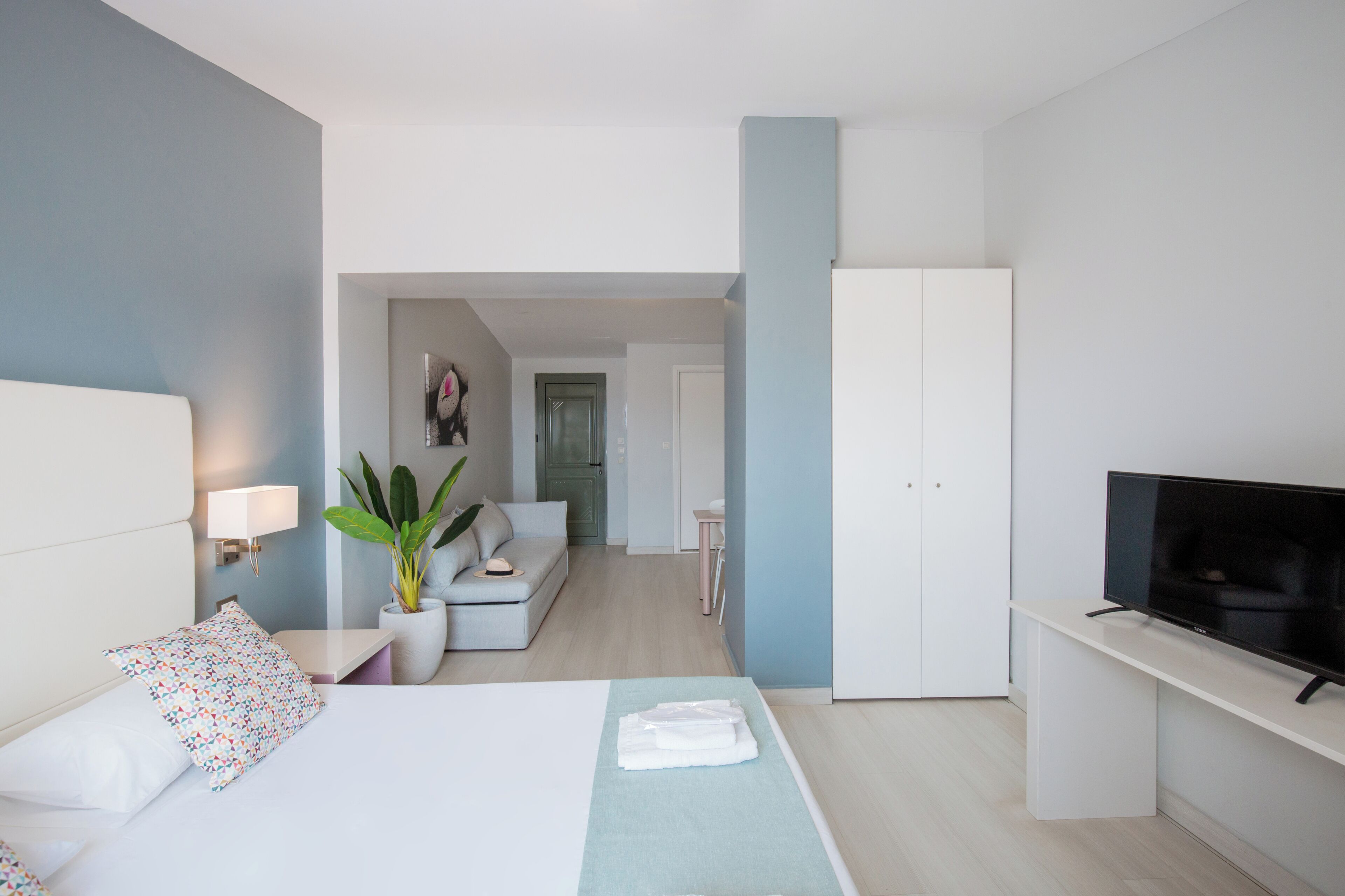 A modern hotel room with a bed, a TV, a desk, and a seating area.