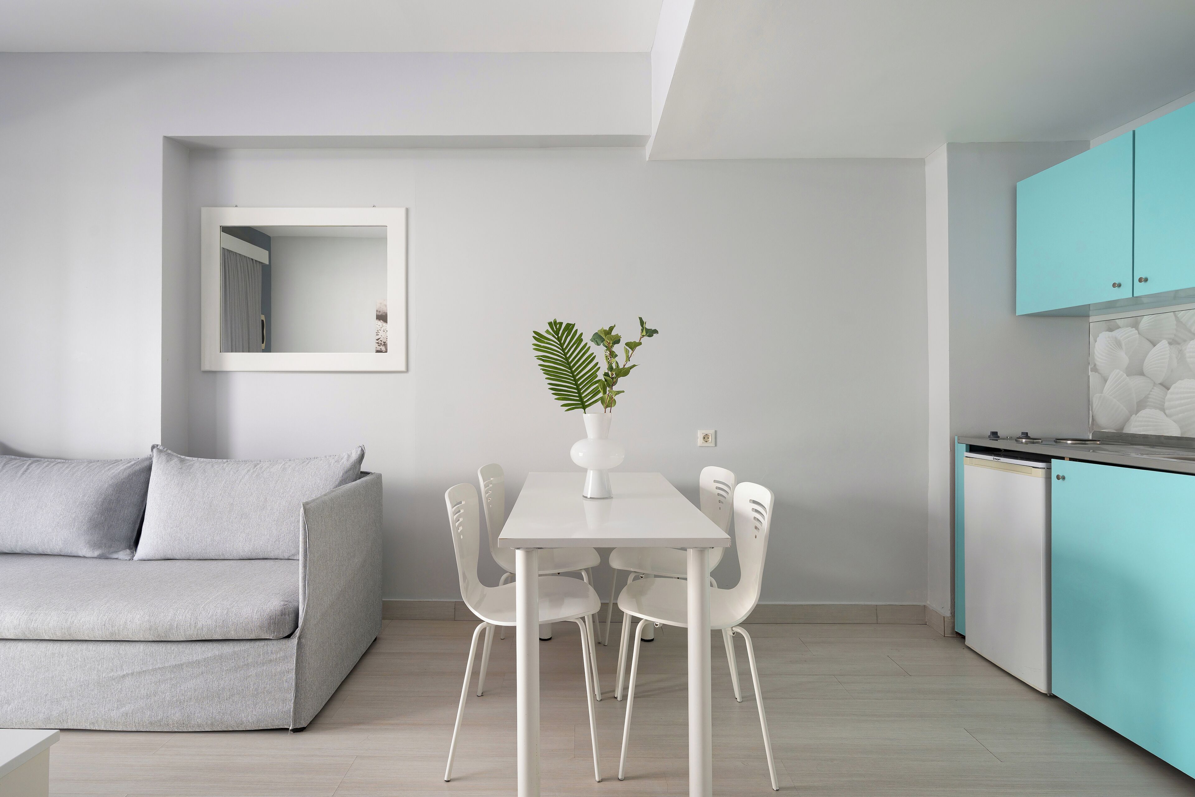 A modern kitchen with white cabinets, a dining table with chairs, and a grey sofa.