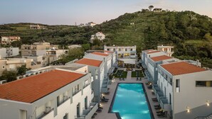 Un hotel moderno con piscina, varios balcones y vistas a las colinas circundantes.