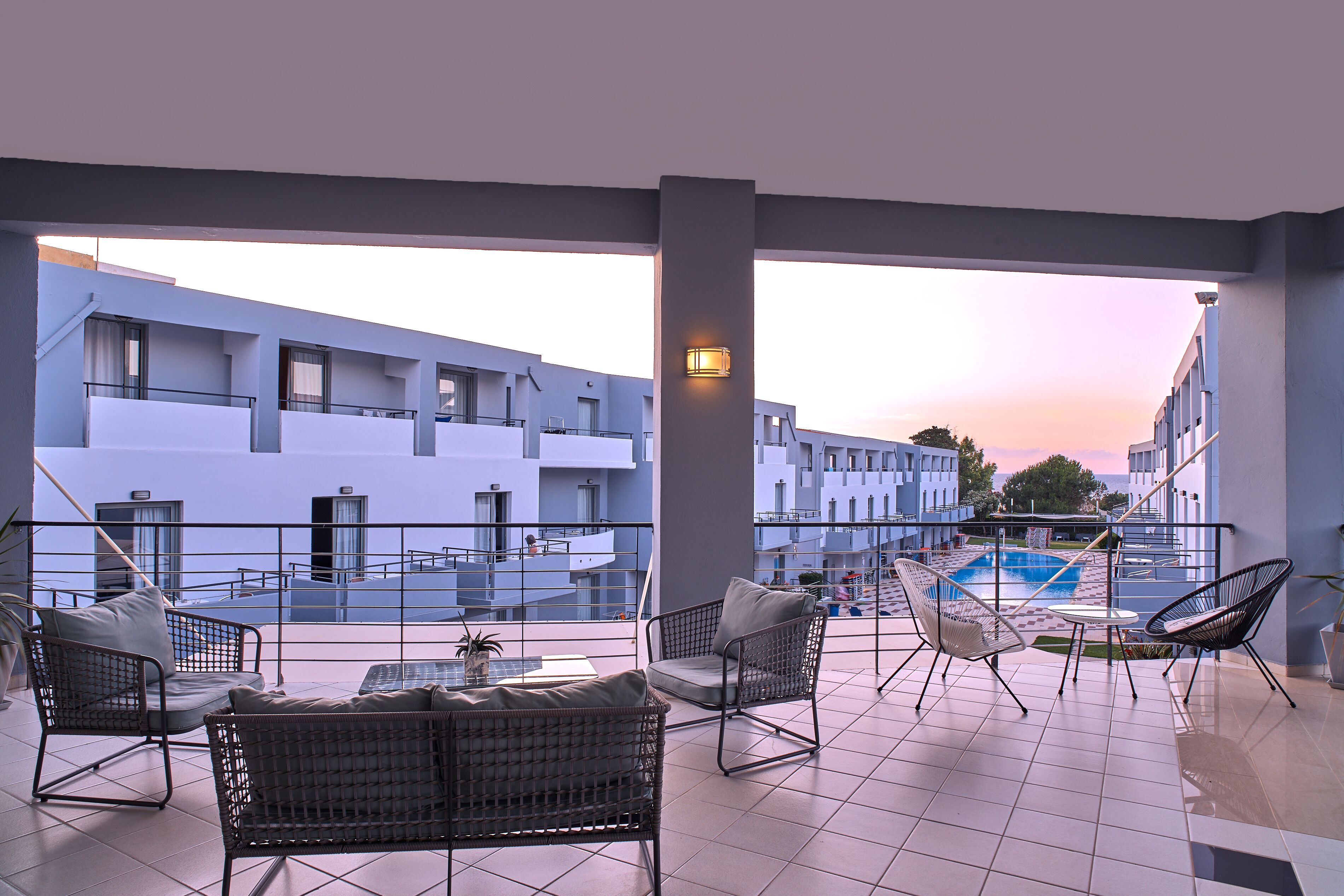 A terrace with wicker furniture, a pool, and a view of a modern building.