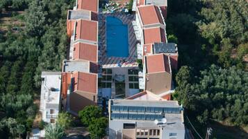 An aerial view of a resort with a central swimming pool, multiple buildings with red roofs, and surrounding greenery.