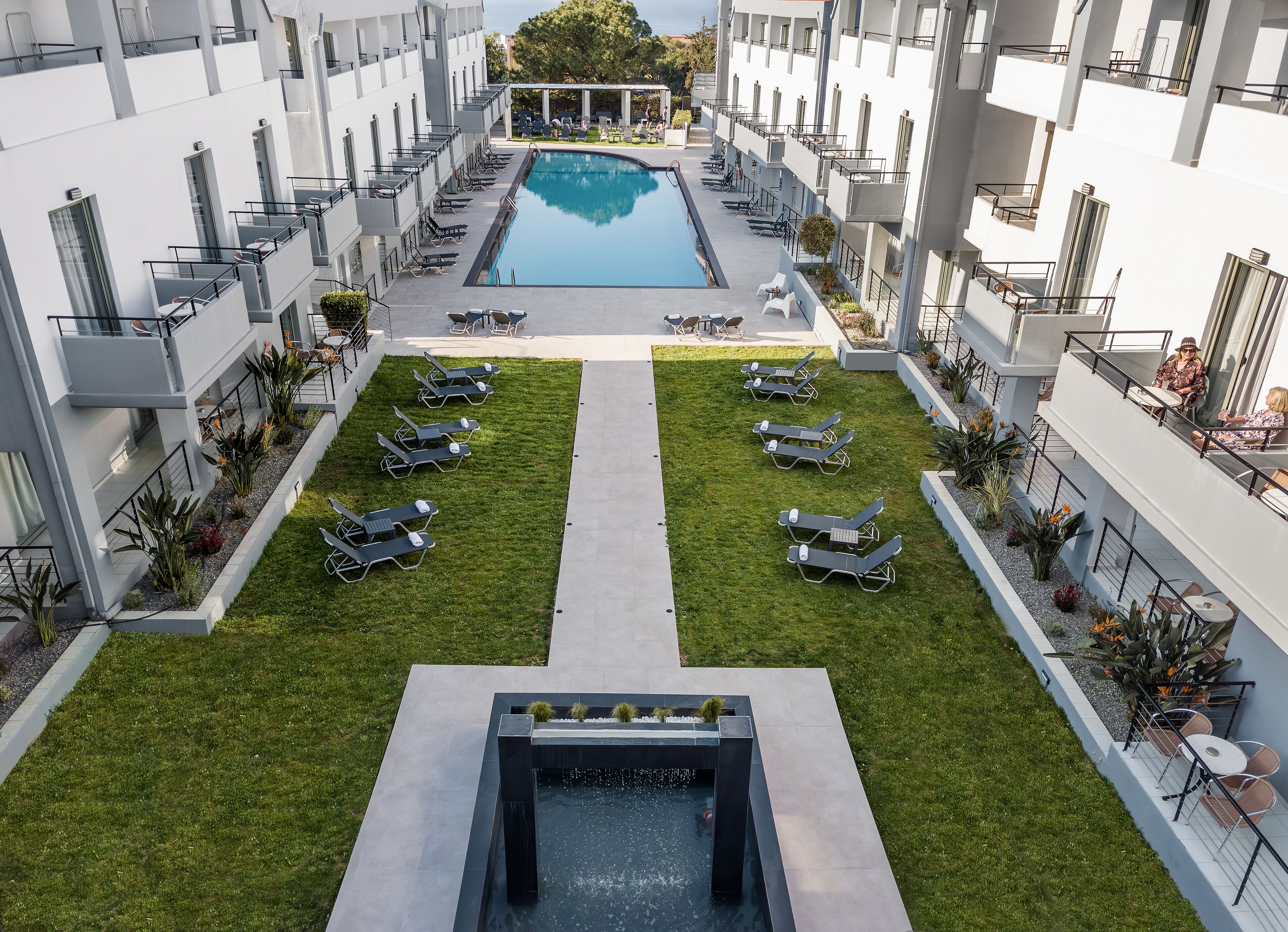 Un hotel moderno con piscina central, tumbonas y césped cuidado.