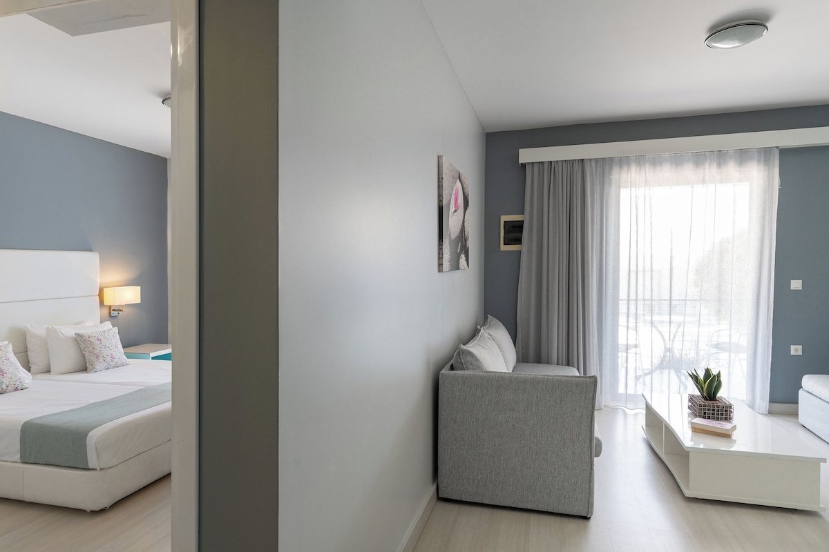A modern hotel room with a bed, a sofa, a coffee table with a plant, and a window with curtains.