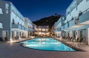 A modern hotel with a swimming pool, multiple balconies, and a view of a hill. - Sunrise Village Hotel (Chania)