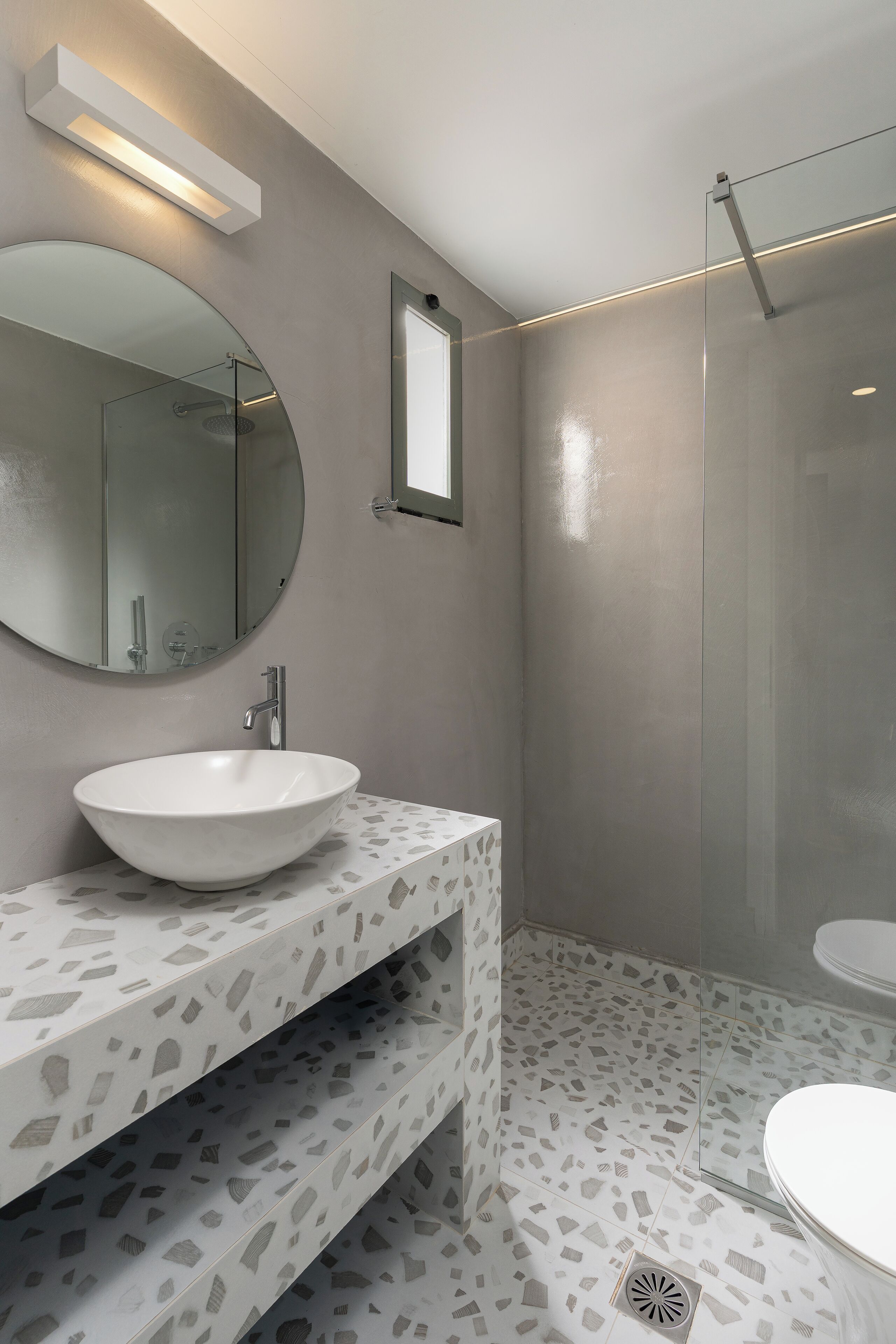 Un baño con un espejo redondo, un lavabo blanco, una ducha y un inodoro.