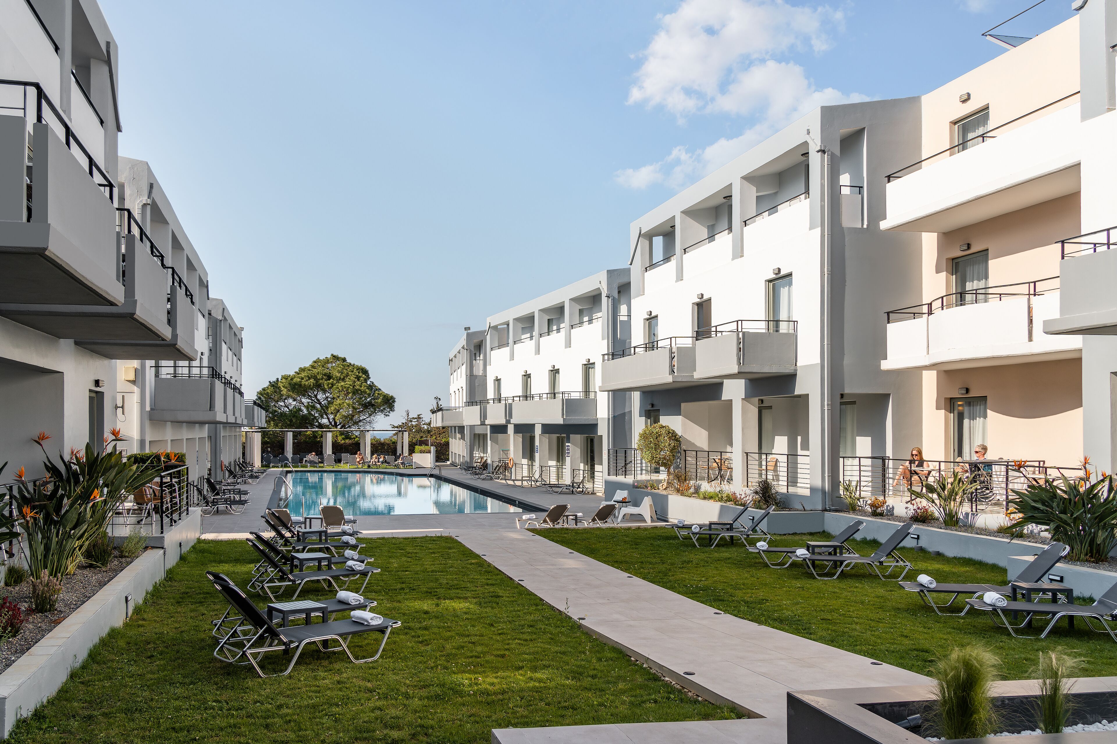 A modern hotel with a swimming pool, sun loungers, and a well-maintained garden.