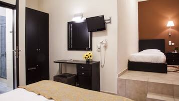 A hotel room with a bed, a desk with a computer monitor, a telephone, and a wall-mounted TV.